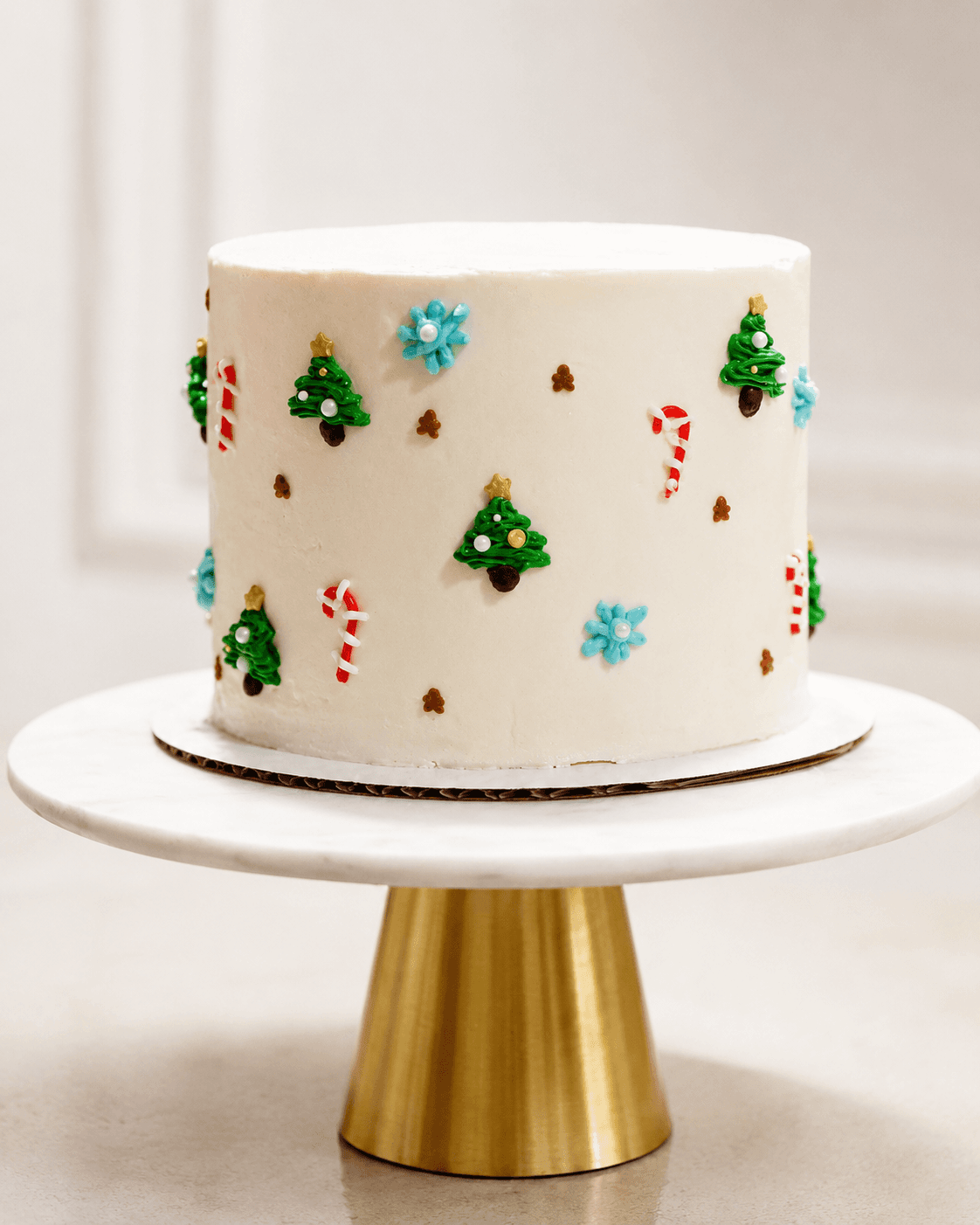 Spilled Milk Cake Boutique - Mini white buttercream cake with piped holiday details displayed on a gold pedestal stand