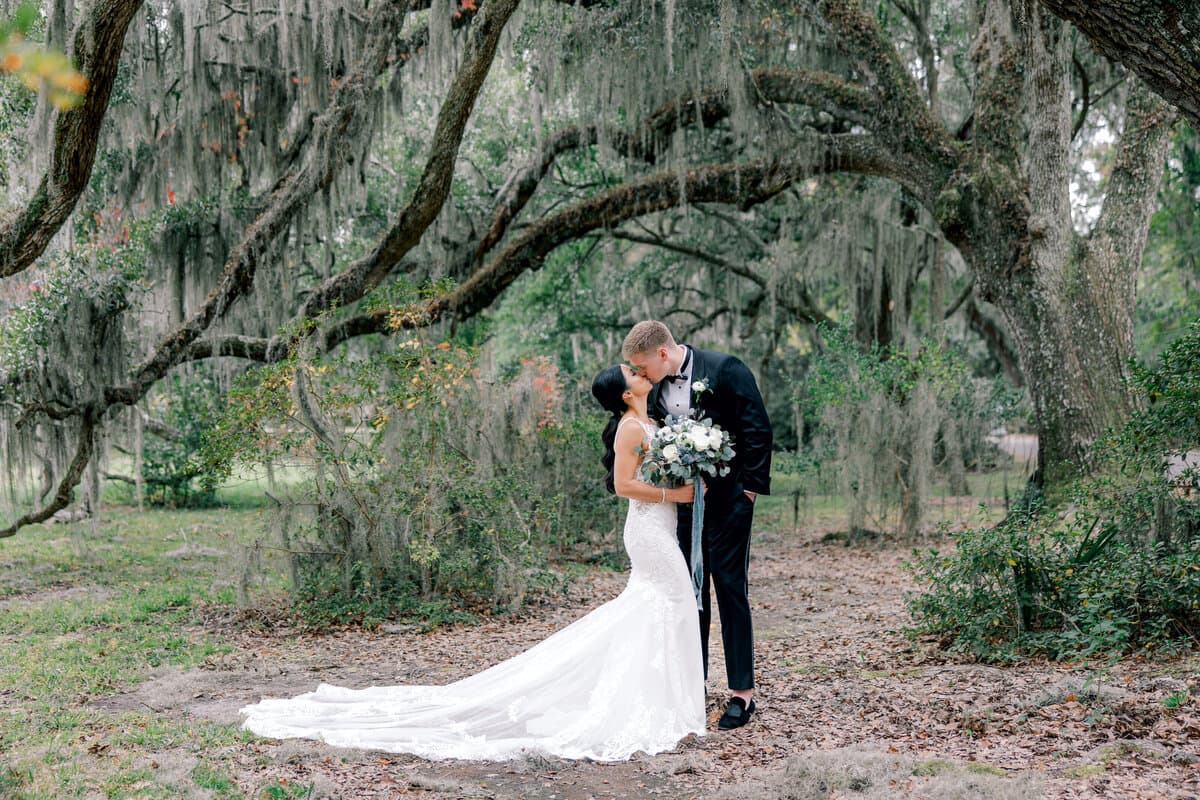 Bride and groom sharing a kiss under sprawling oak trees