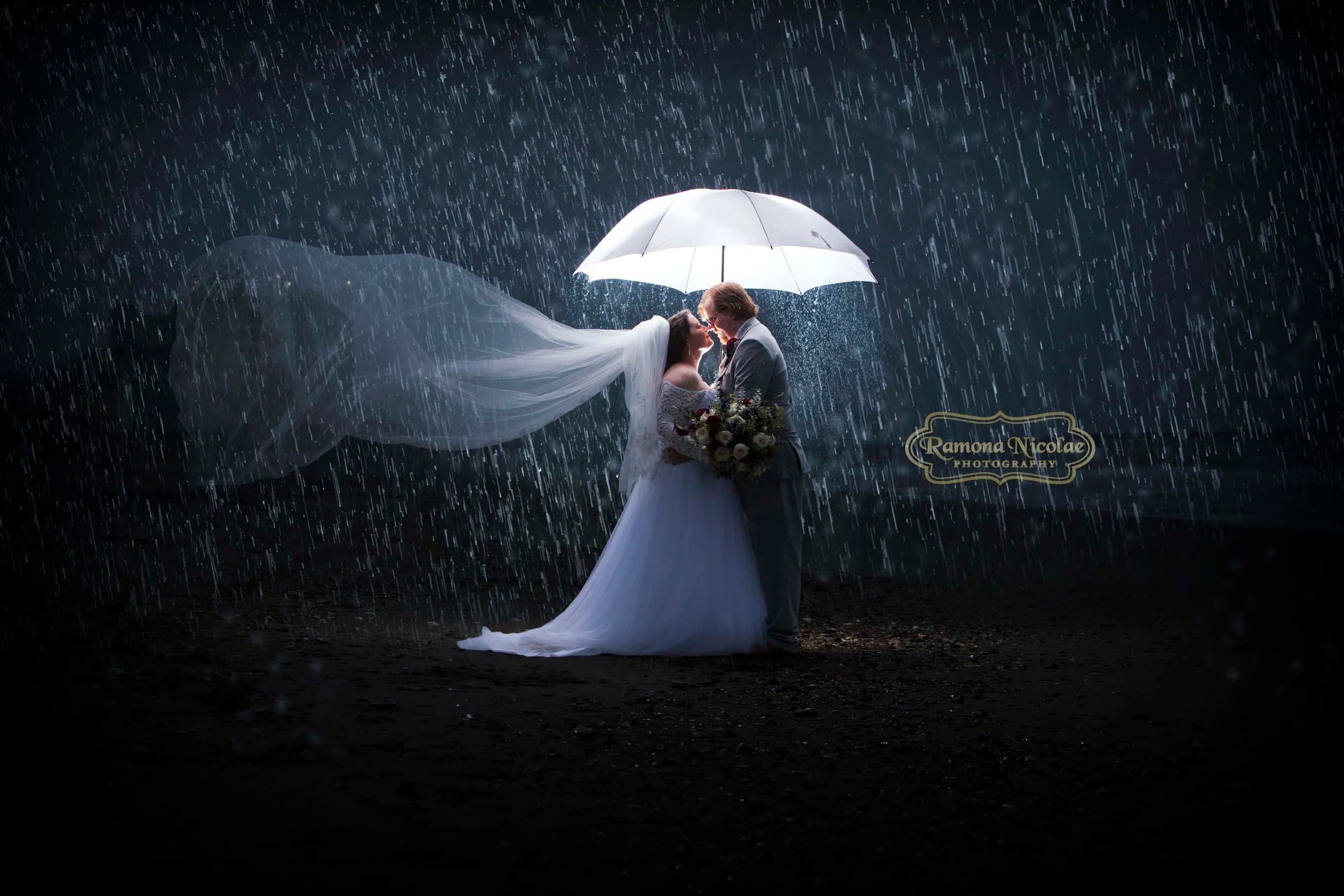 Bride and groom embracing under a lit umbrella in the rain in Myrtle Beach